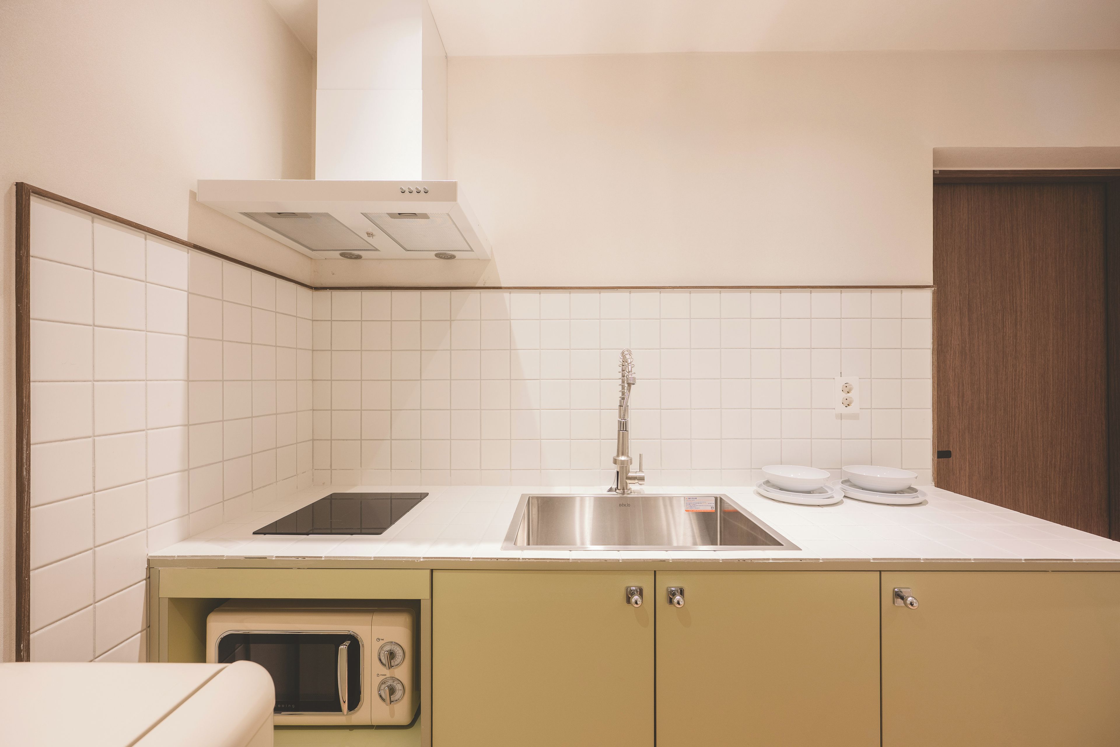 Una cocina compacta con microondas integrado, un lavamanos de acero inoxidable y un horno pequeño.