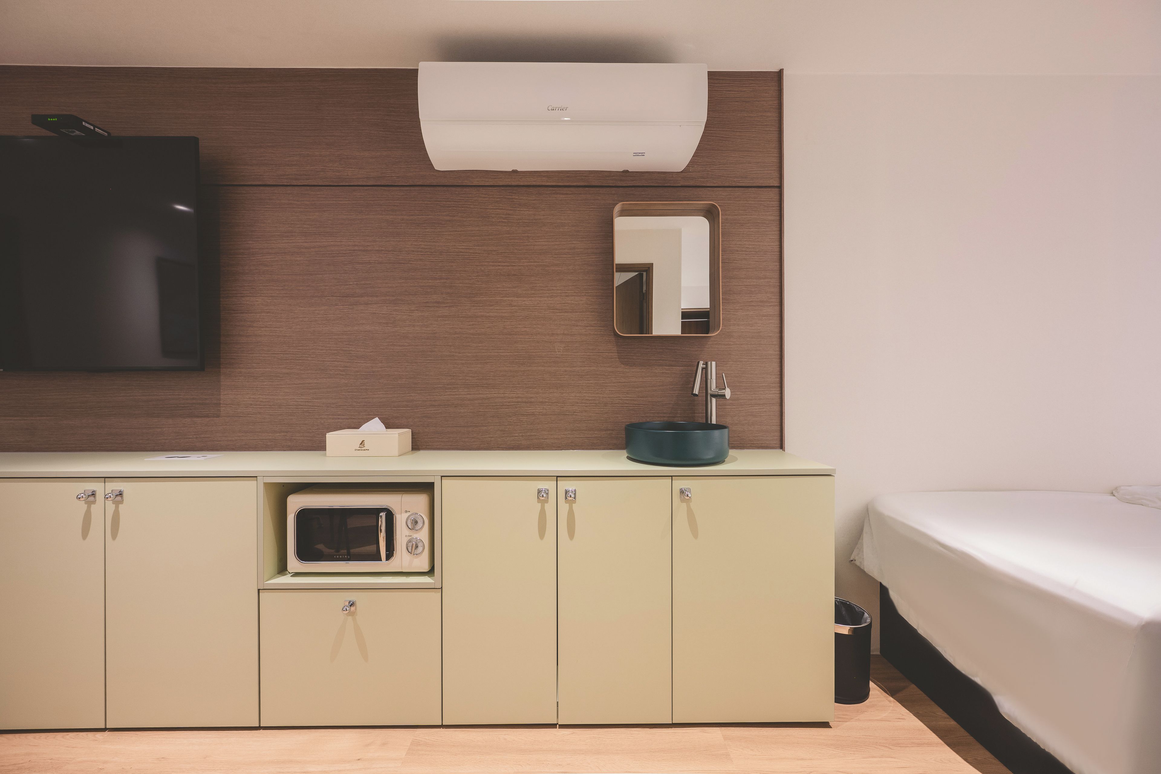 Una habitación de hotel moderna con kitchenette, una cama, un espejo y un equipo de aire acondicionado.