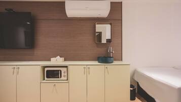 Una habitación de hotel moderna con kitchenette, una cama, un espejo y un equipo de aire acondicionado.