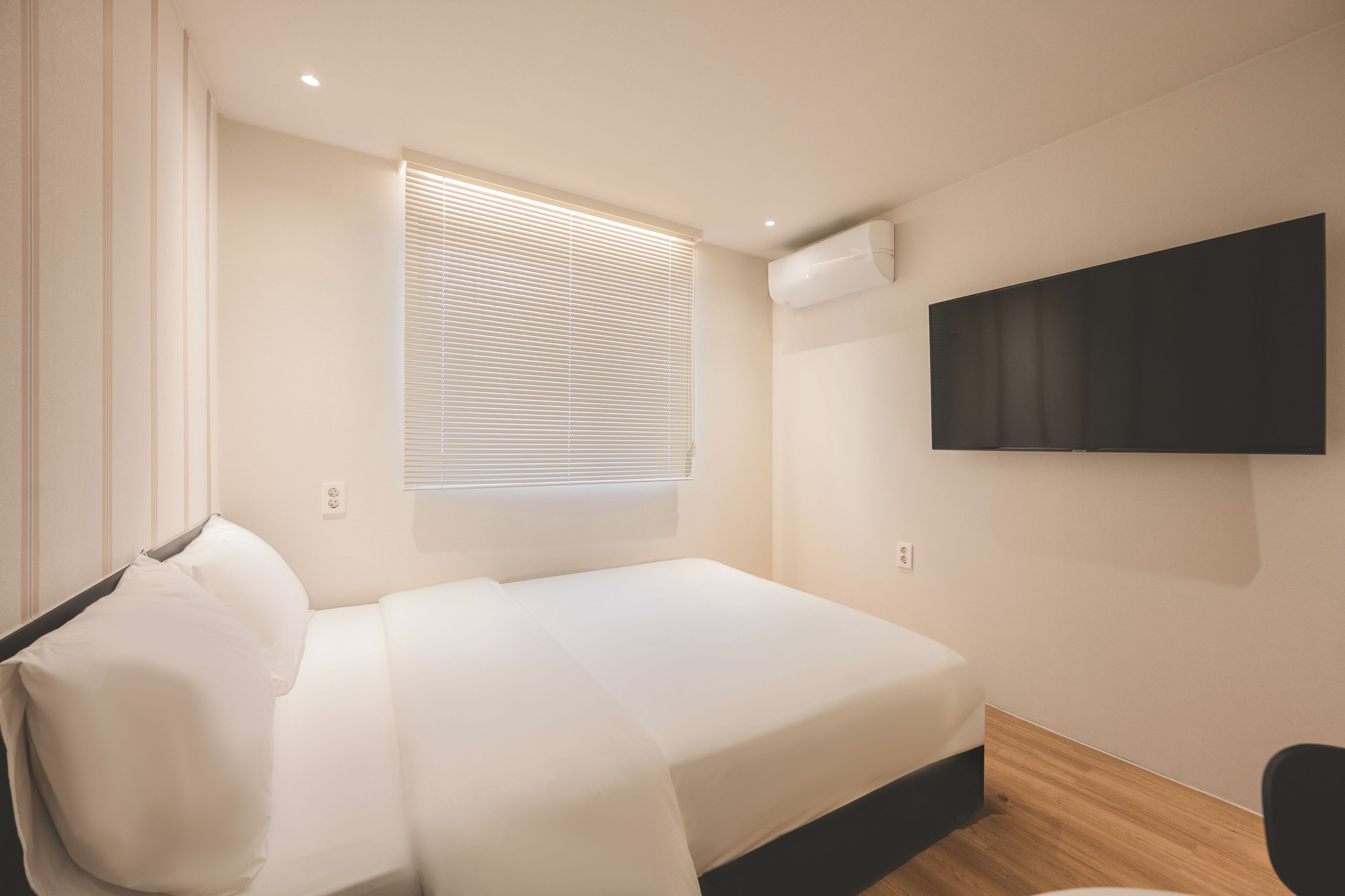 Habitación de hotel moderna con una cama, un televisor de pantalla plana montado en la pared y una ventana con persianas.