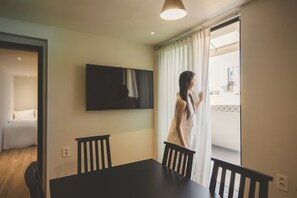 Habitación de hotel con una mesa de comedor, sillas, un televisor montado en la pared y vistas al exterior.