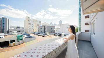 A balcony with a tiled floor and a view of a parking lot and buildings.