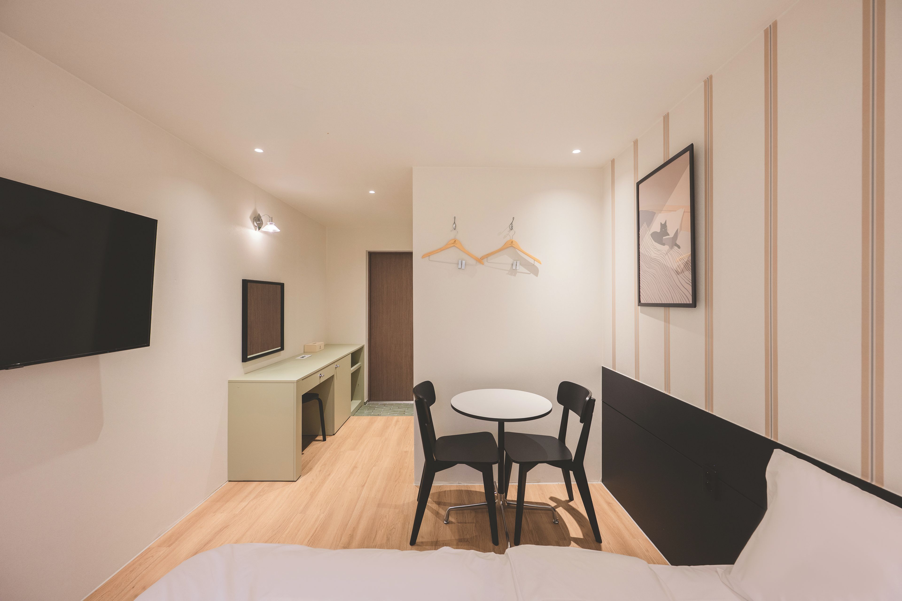 A hotel room with a bed, a desk, a chair, a TV, and a painting on the wall.