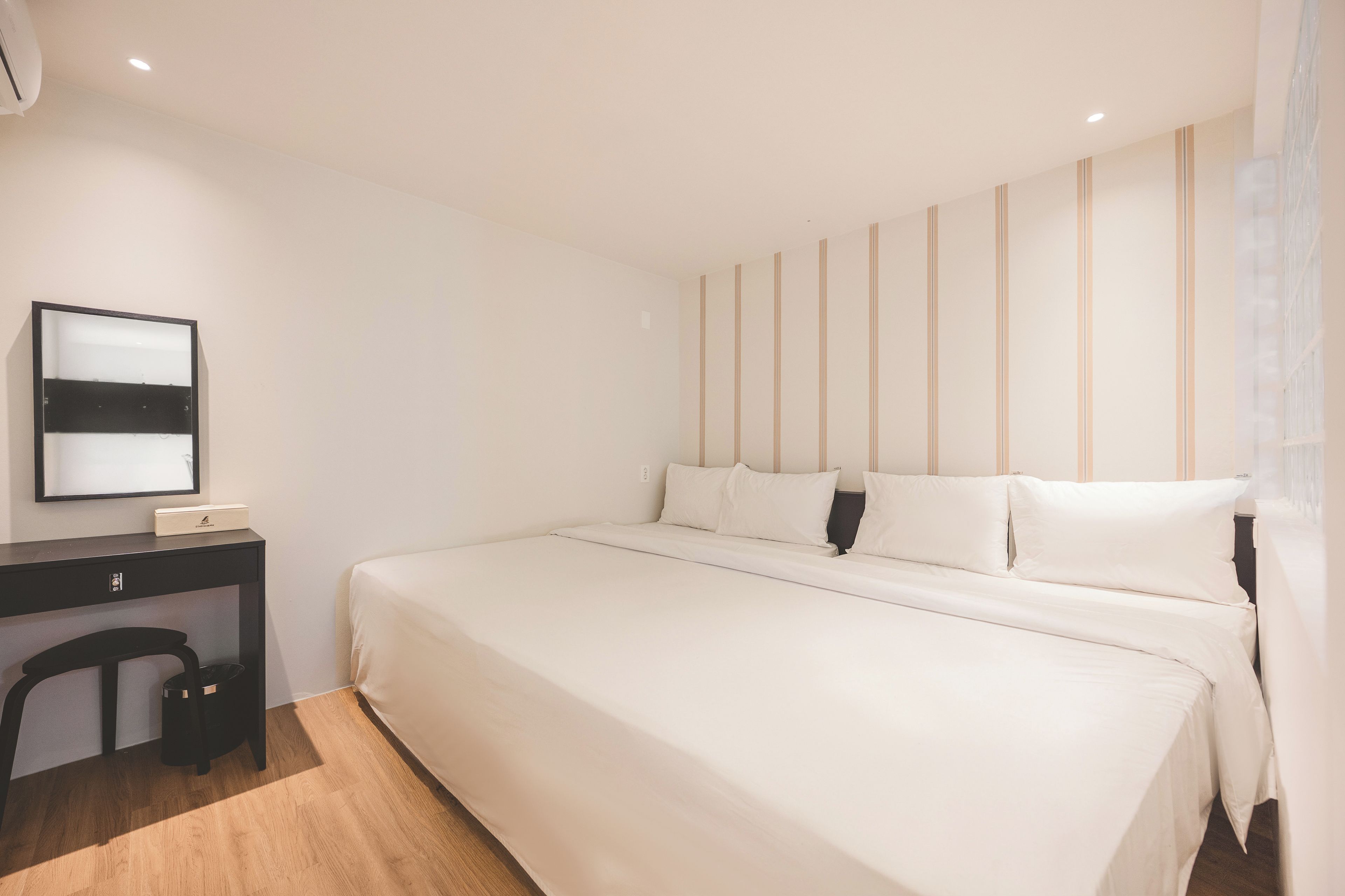 Et hotelværelse med en stor seng, et skrivebord med stol og en vægmonteret aircondition.
