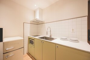 Una cucina compatta con forno a microonde integrato, lavello in acciaio inossidabile e frigorifero compatto.