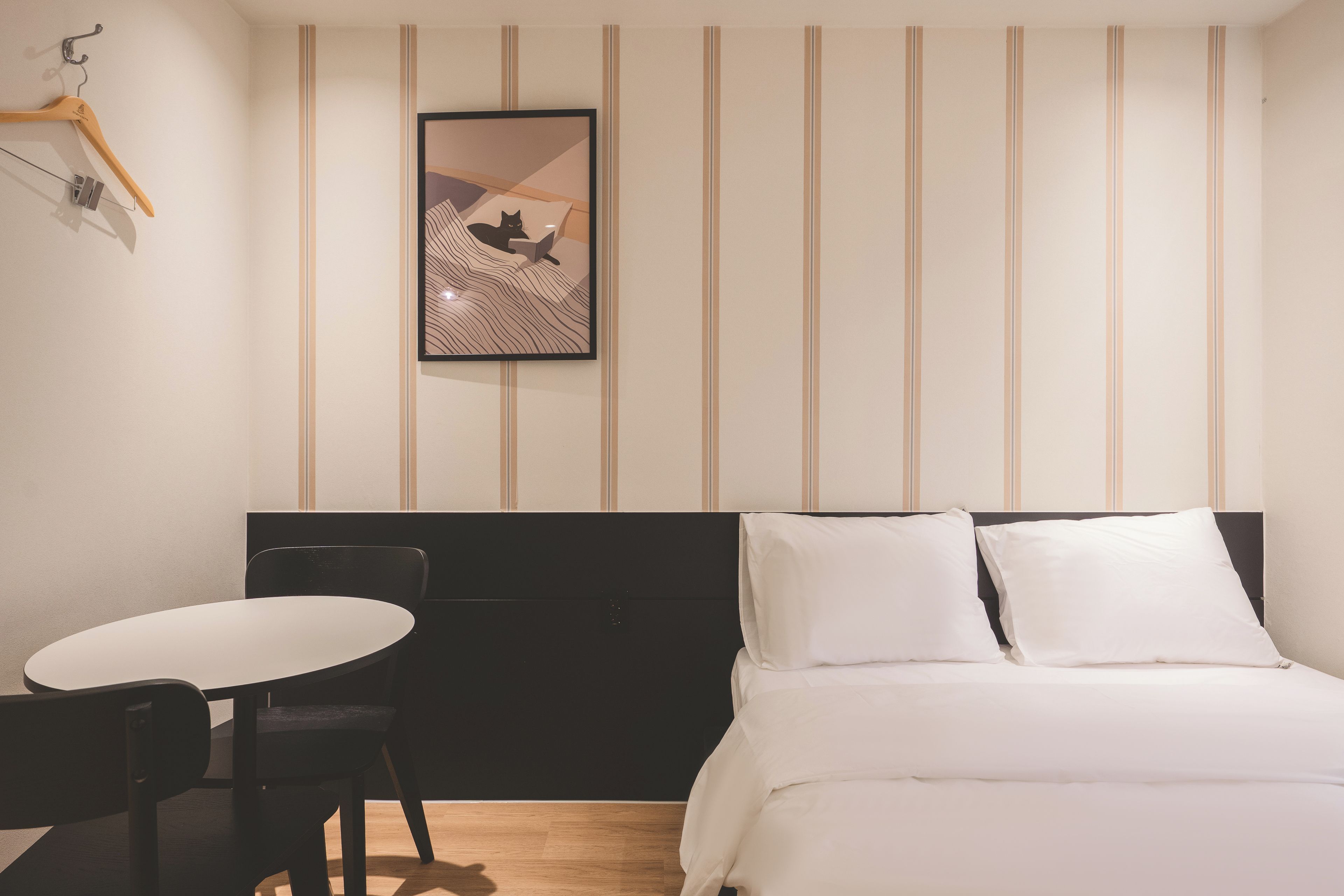 Une chambre d’hôtel avec un lit, un bureau et une chaise. Un tableau encadré est accroché au mur.