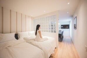 Un dormitorio con dos camas, un ventanal con paneles decorativos y una zona de comedor con televisor.