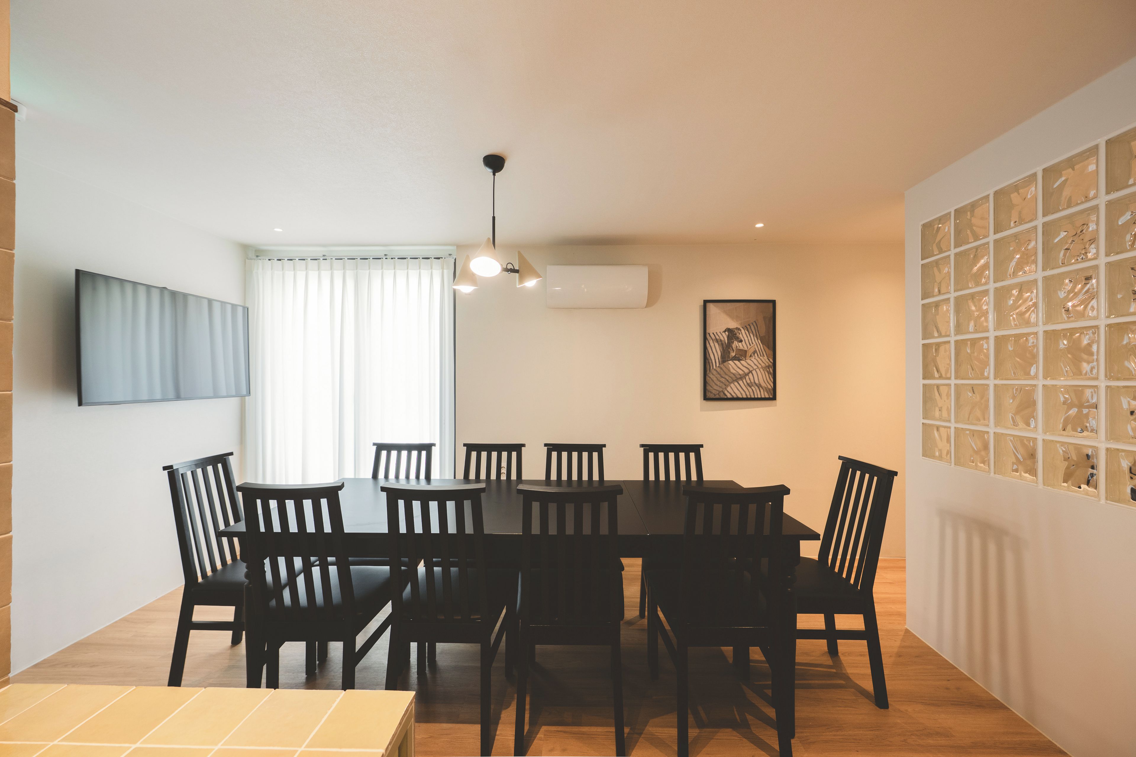 A dining area with a table and chairs, an air conditioning unit, a window with curtains, and a wall with a patterned design.
