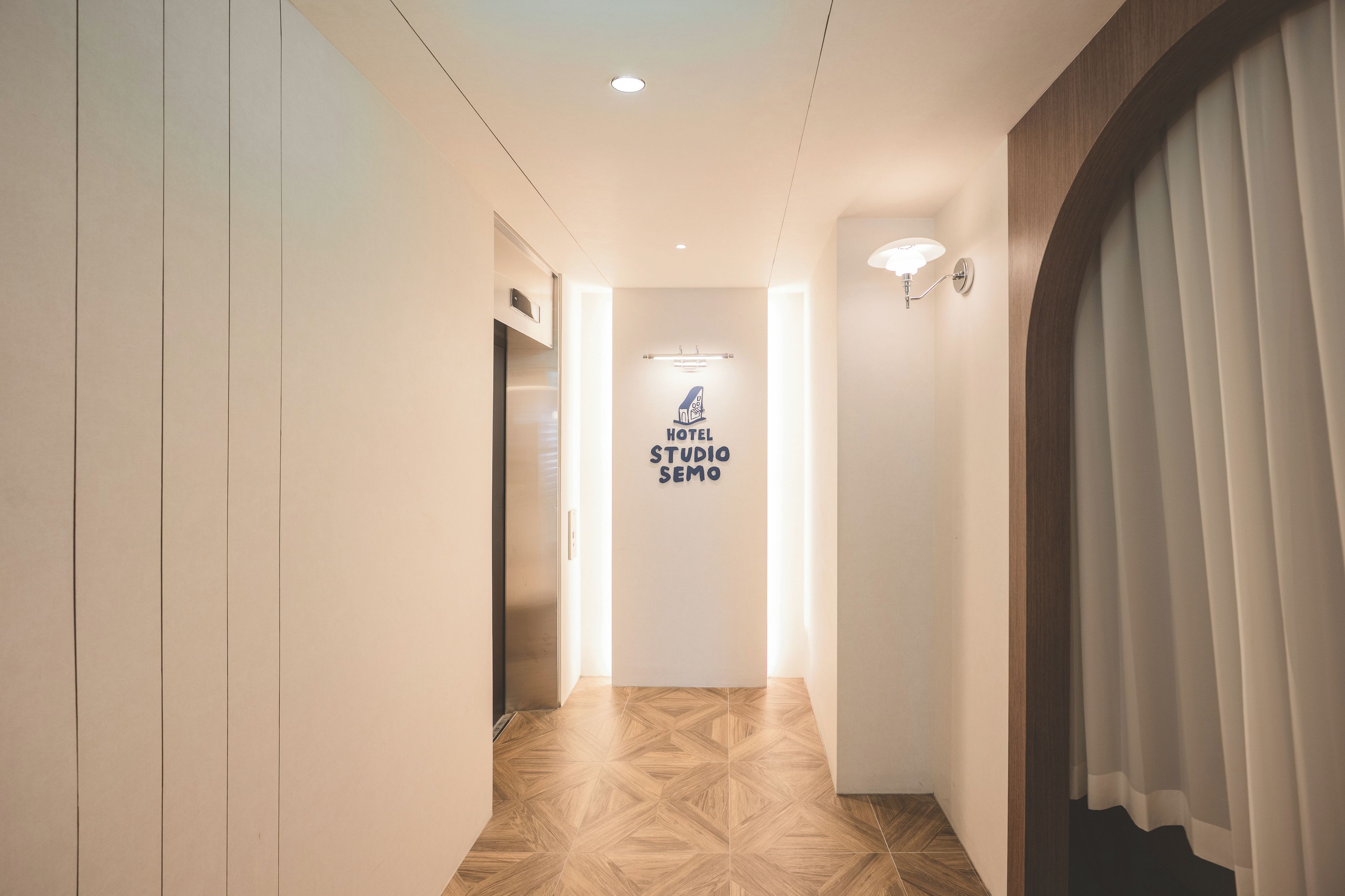 Ein Hotelkorridor mit einem Schild, auf dem 'HOTEL STUDIO SEMO' steht, und einem modernen Aufzug.
