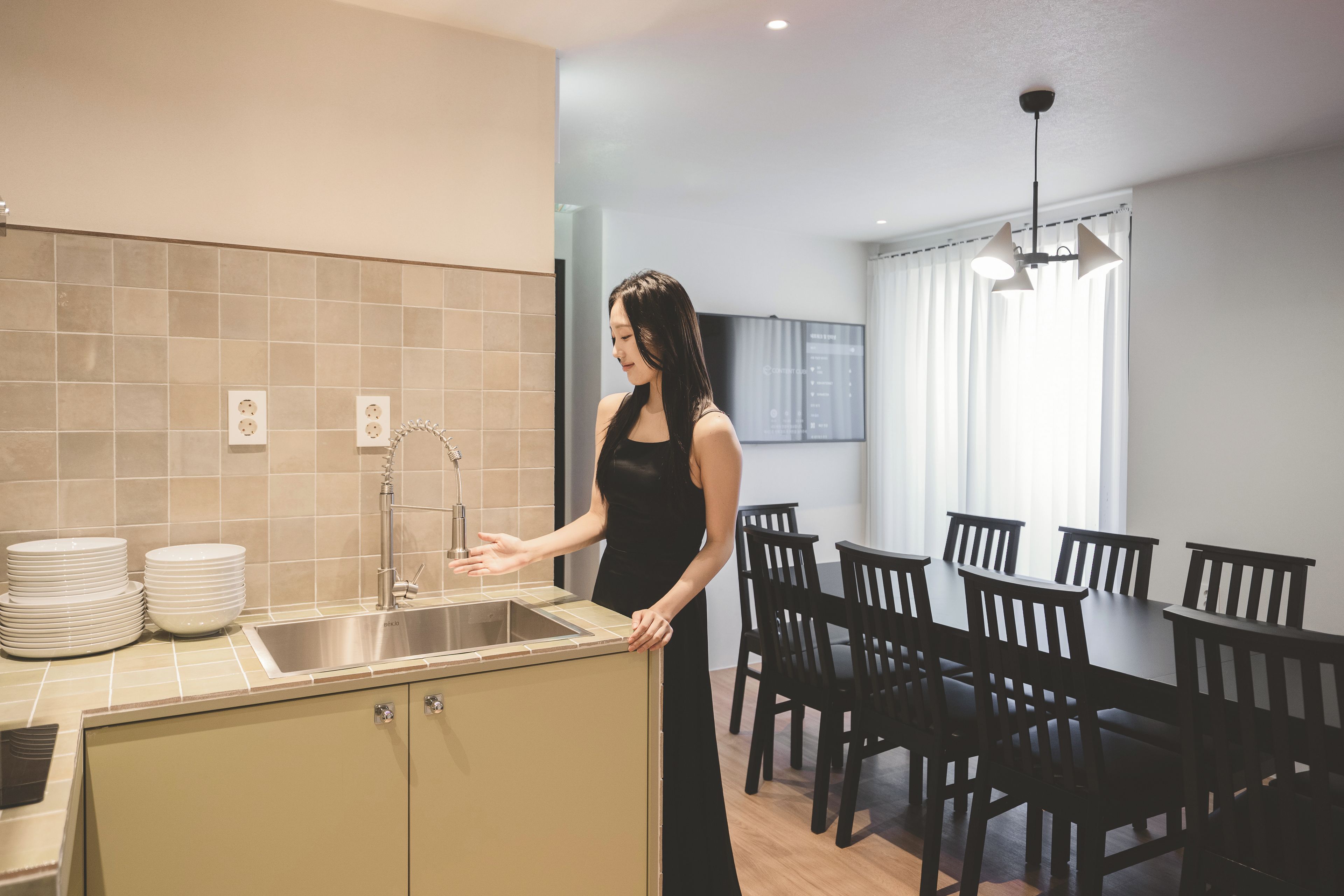 A modern kitchen with a sink, a dining area with chairs and a table, and a ceiling light fixture.
