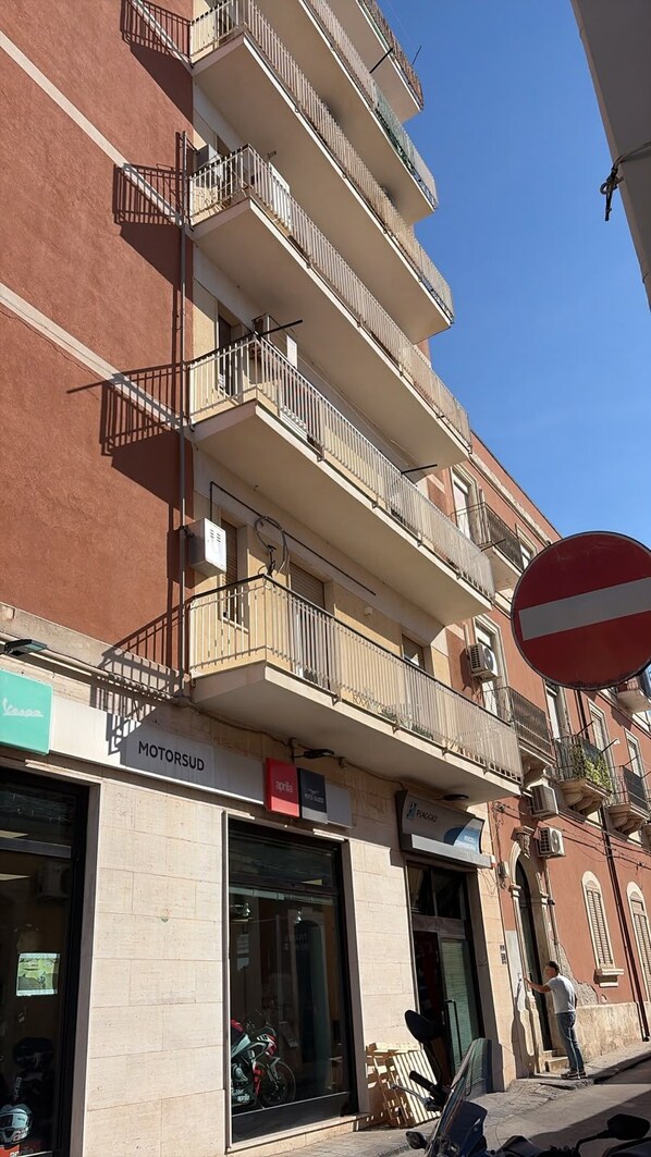 A multi-story building with balconies, a visible 'MOTORSUD' sign, and a 'PIAGGO' sign.