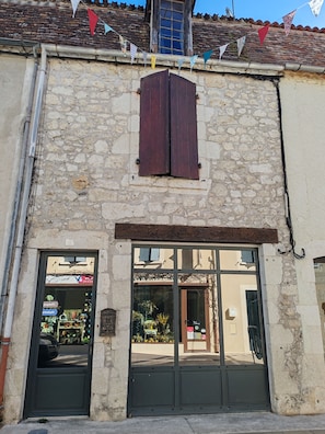 A stone building with a wooden shuttered window, a metal door, and a shop with glass display windows. - A charming house in downtown Eymet, ideal for 6 people. (Eymet)