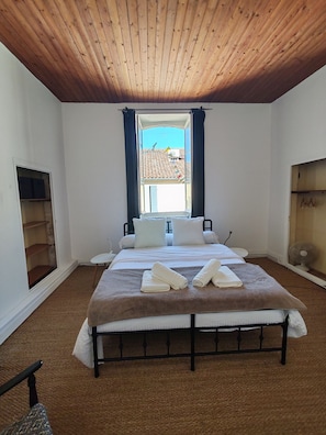 A bedroom with a wooden ceiling, a large bed with white bedding, a window with curtains, and a small table. - A charming house in downtown Eymet, ideal for 6 people. (Eymet)