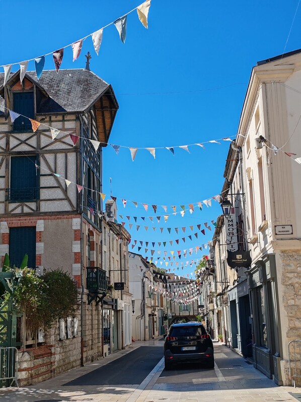 Une rue étroite bordée de bâtiments traditionnels à colombages, une voiture garée et des drapeaux triangulaires colorés tendus au-dessus de la rue.