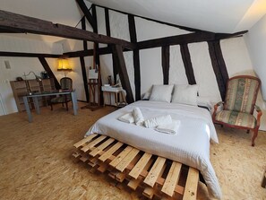 Une chambre avec un plancher en bois, un lit avec une literie blanche, un bureau en bois, une chaise et une chaise en bois avec un coussin à motifs.