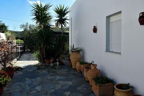 A stone-paved courtyard with potted plants and a white wall. - Vrbo Property (Skouloufia)