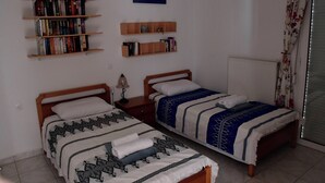 A bedroom with two single beds, a bookshelf, a small table with a lamp, and a window with curtains. - Vrbo Property (Skouloufia)