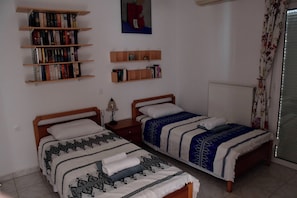 A bedroom with two single beds, a bookshelf, a small table with a lamp, and a window with curtains. - Vrbo Property (Skouloufia)