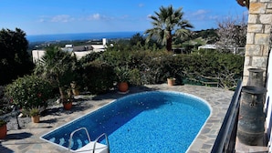 A swimming pool with a view of the sea, surrounded by greenery and stone architecture. - Vrbo Property (Skouloufia)