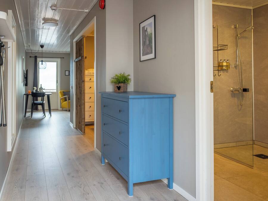 A hotel corridor with a blue dresser, a shower room, and a dining area with a yellow chair.