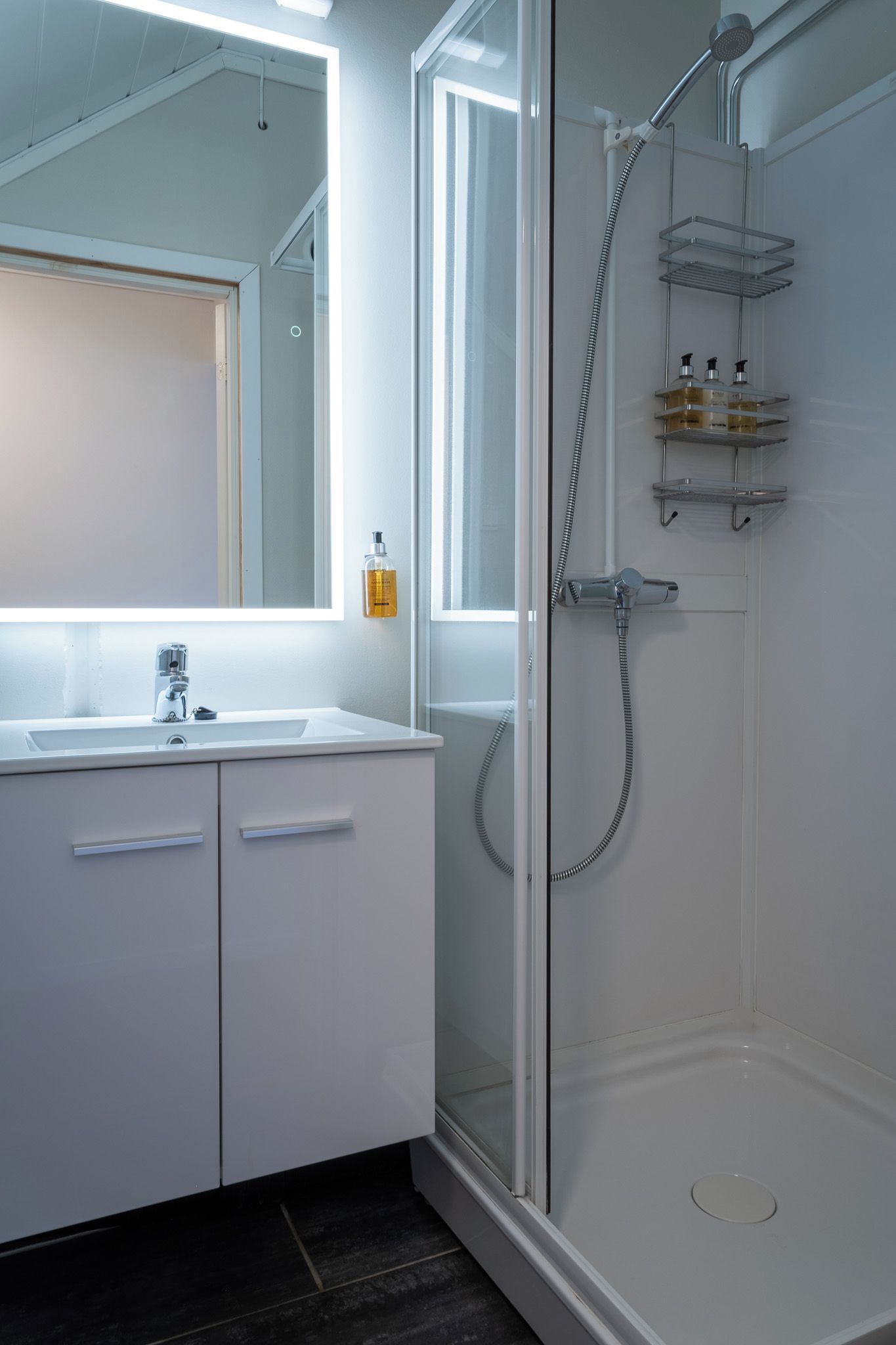 Un baño moderno con ducha envuelta en vidrio, muebles blancos y un espejo grande.