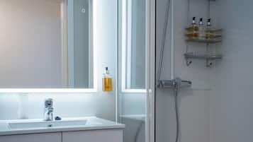 Un baño moderno con ducha envuelta en vidrio, muebles blancos y un espejo grande.