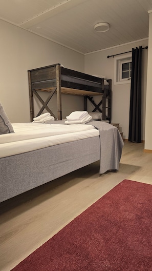 A bunk bed with a grey mattress and pillows, a red rug, and a window with curtains.