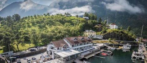 A coastal building with a dock, boats, and a mountainous backdrop.