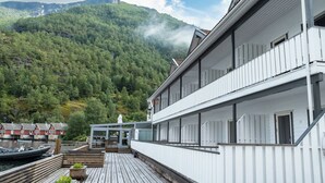 A waterfront property with a wooden deck, a glass structure, and a view of a forested mountain. - Flåm Marina (Flåm)