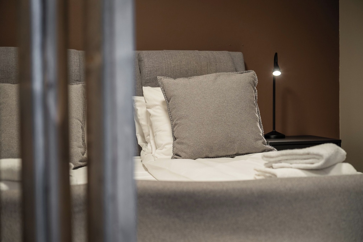 A neatly made bed with pillows and a folded towel, a bedside lamp, and a wall with a textured finish.