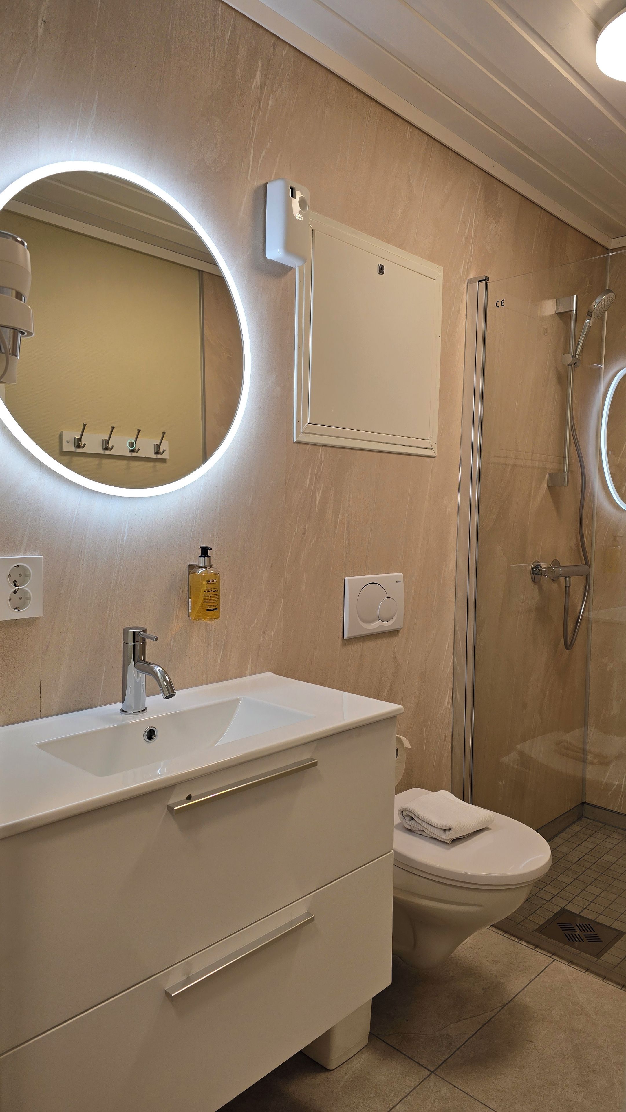 A modern bathroom with a white vanity, a round mirror, a handheld showerhead, and a toilet.