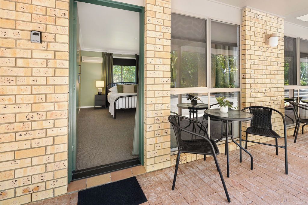 A hotel room with a bed, a small table, and a chair. There is a window with a view of trees.