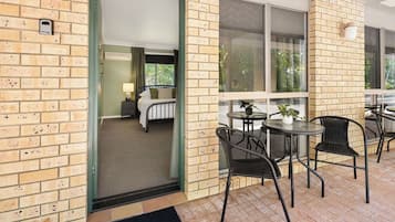 A hotel room with a bed, a small table, and a chair. There is a window with a view of trees.