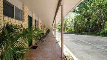A covered outdoor area with a brick wall, potted plants, and a paved walkway.
