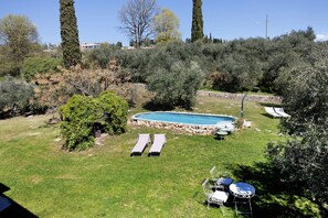 A backyard with a swimming pool, two lounge chairs, a barbecue grill, and a stone wall. - Room 'Camera 7 - Economy Ampia' with Shared Pool, Wi-Fi and Air Conditioning (Cavaion Veronese)