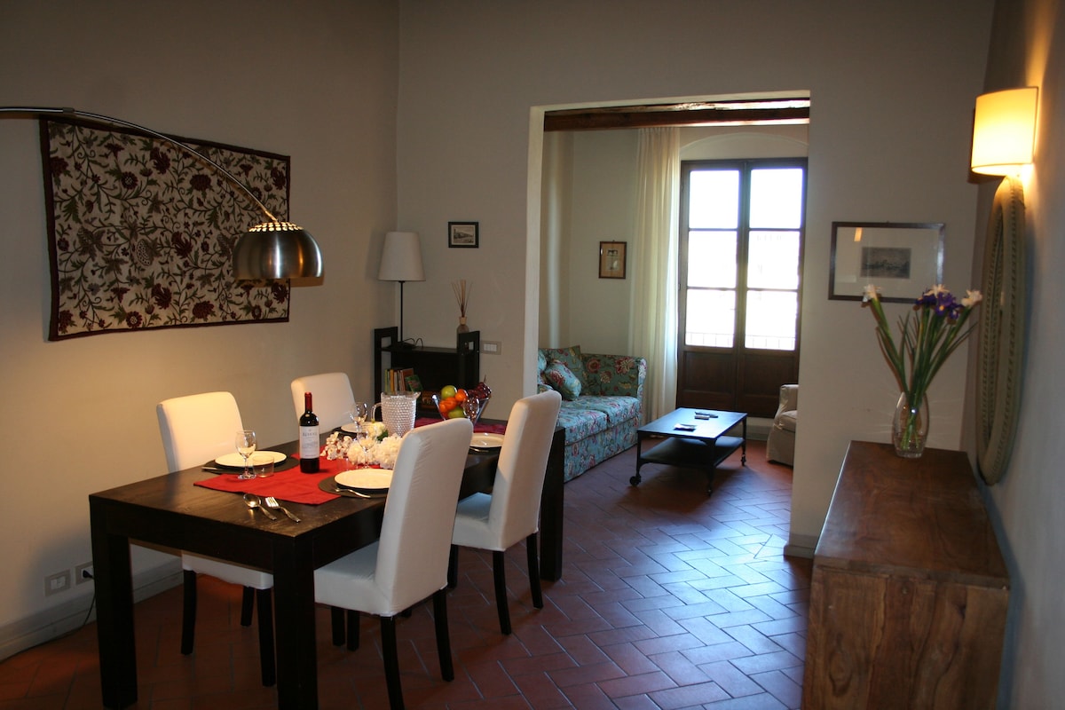 Un comedor con una mesa preparada para dos, un sofá y un ventanal con cortinas.