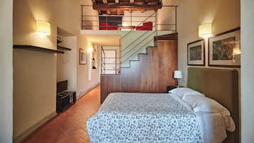 Une chambre d’hôtel avec un lit, un bureau, une chaise, un escalier et un mur orné de tableaux.