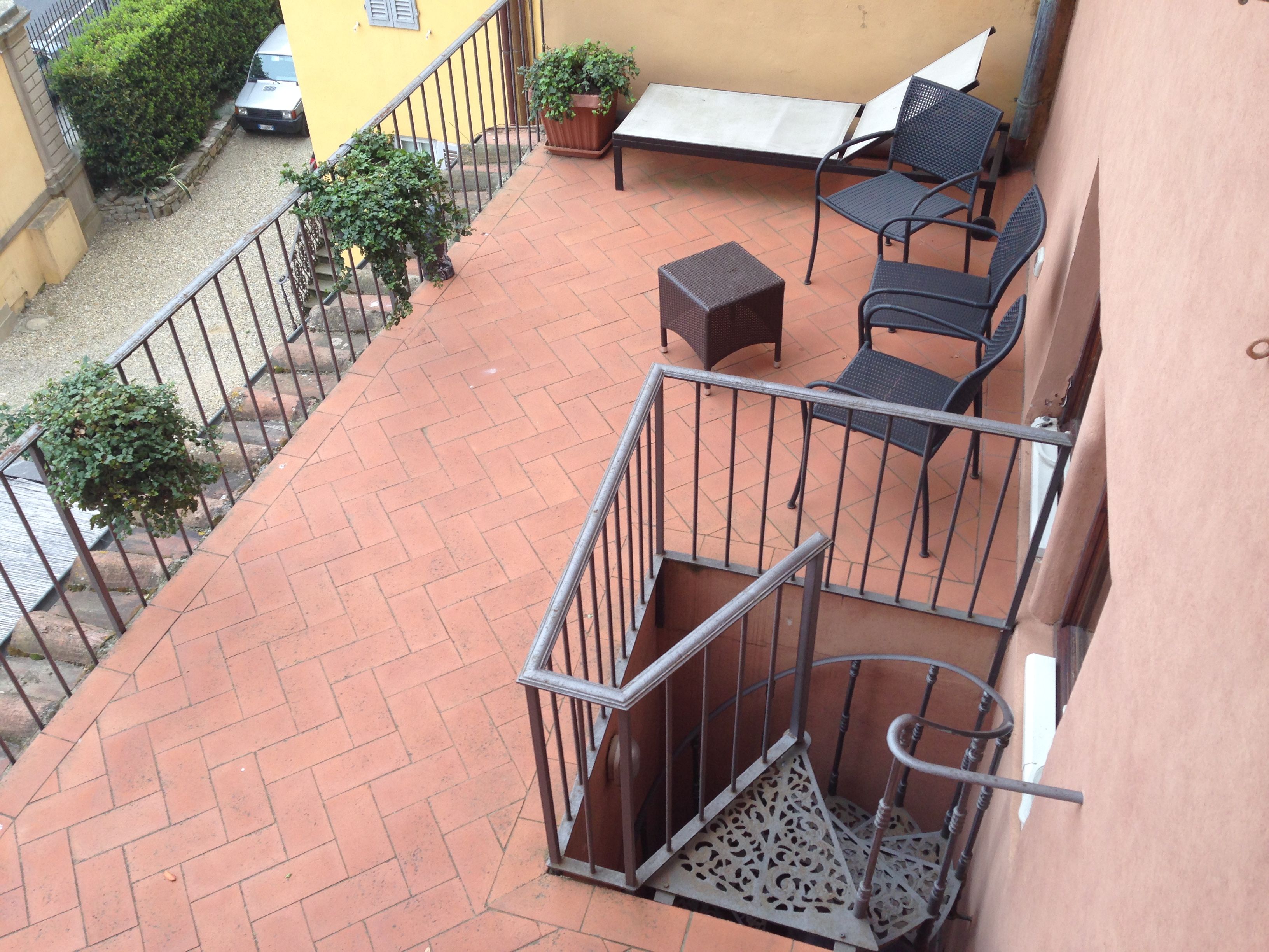 A balcony with a tiled floor, metal railing, a small table, two chairs, and a potted plant.