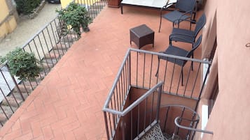A balcony with a tiled floor, metal railing, a small table, two chairs, and a potted plant.