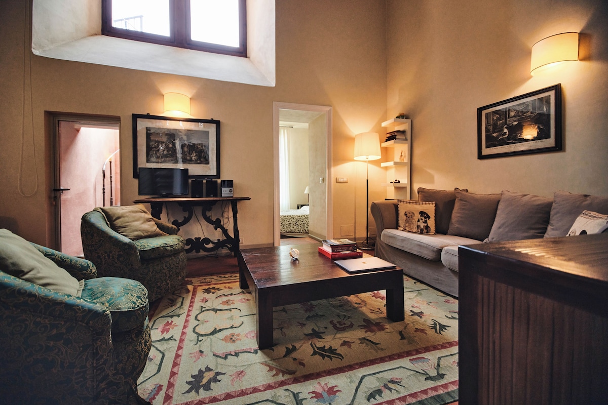 Una sala de estar acogedora con sofá, sillón, mesa de centro y televisor. Hay una ventana, una puerta y una lámpara.