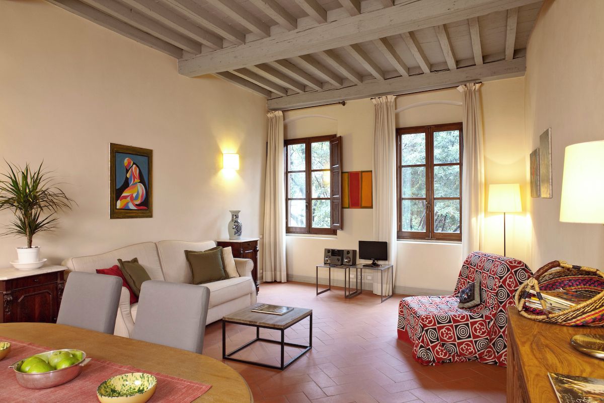Una sala de estar con un sofá, una mesa de centro, una mesa de comedor con tazones, un televisor sobre un mueble bajo y una silla estampada.