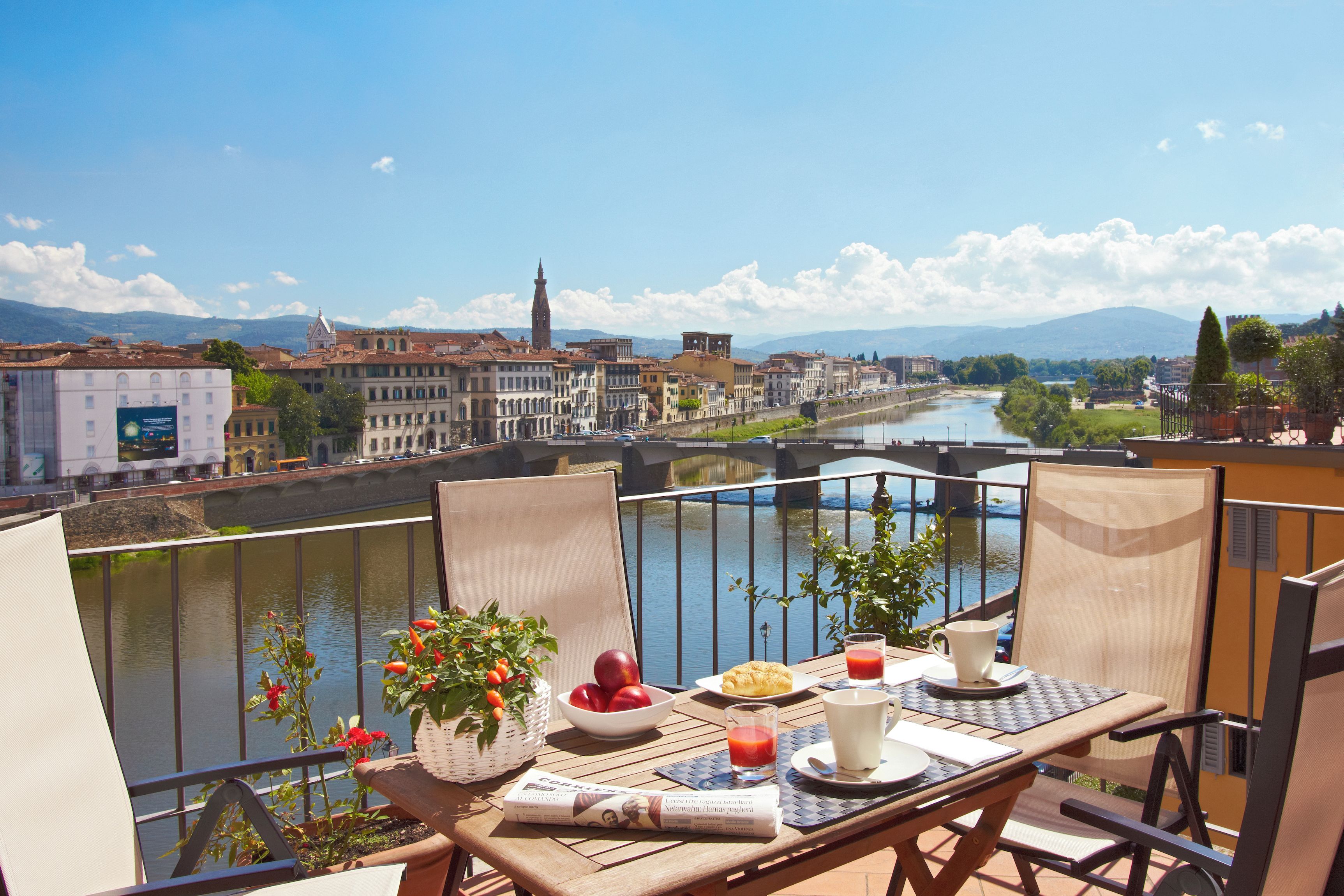 A balcony with a table set for breakfast overlooking a river and historic buildings.