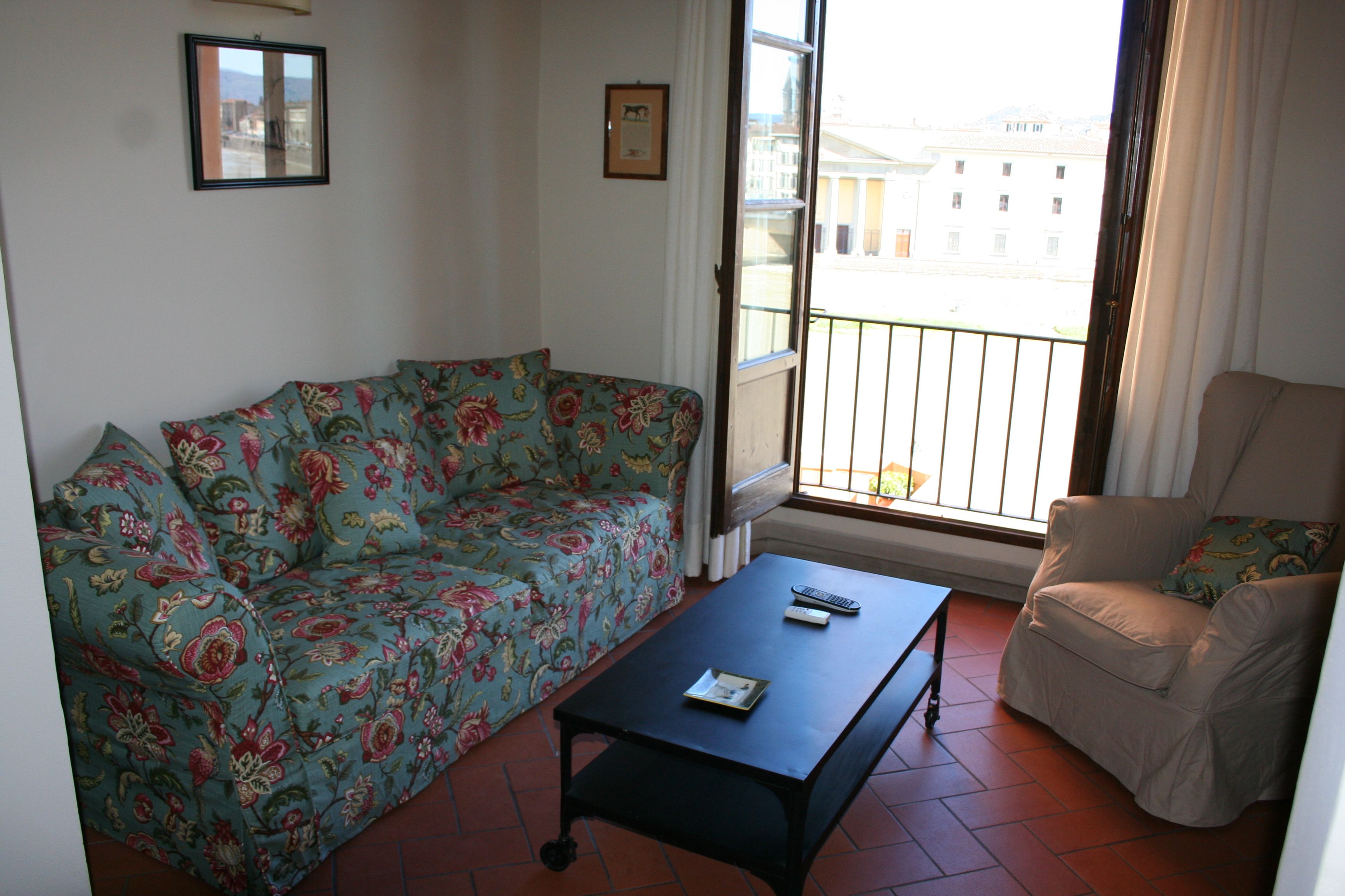 Una sala de estar con sofá, una silla, una mesa de centro y un balcón con barandilla.