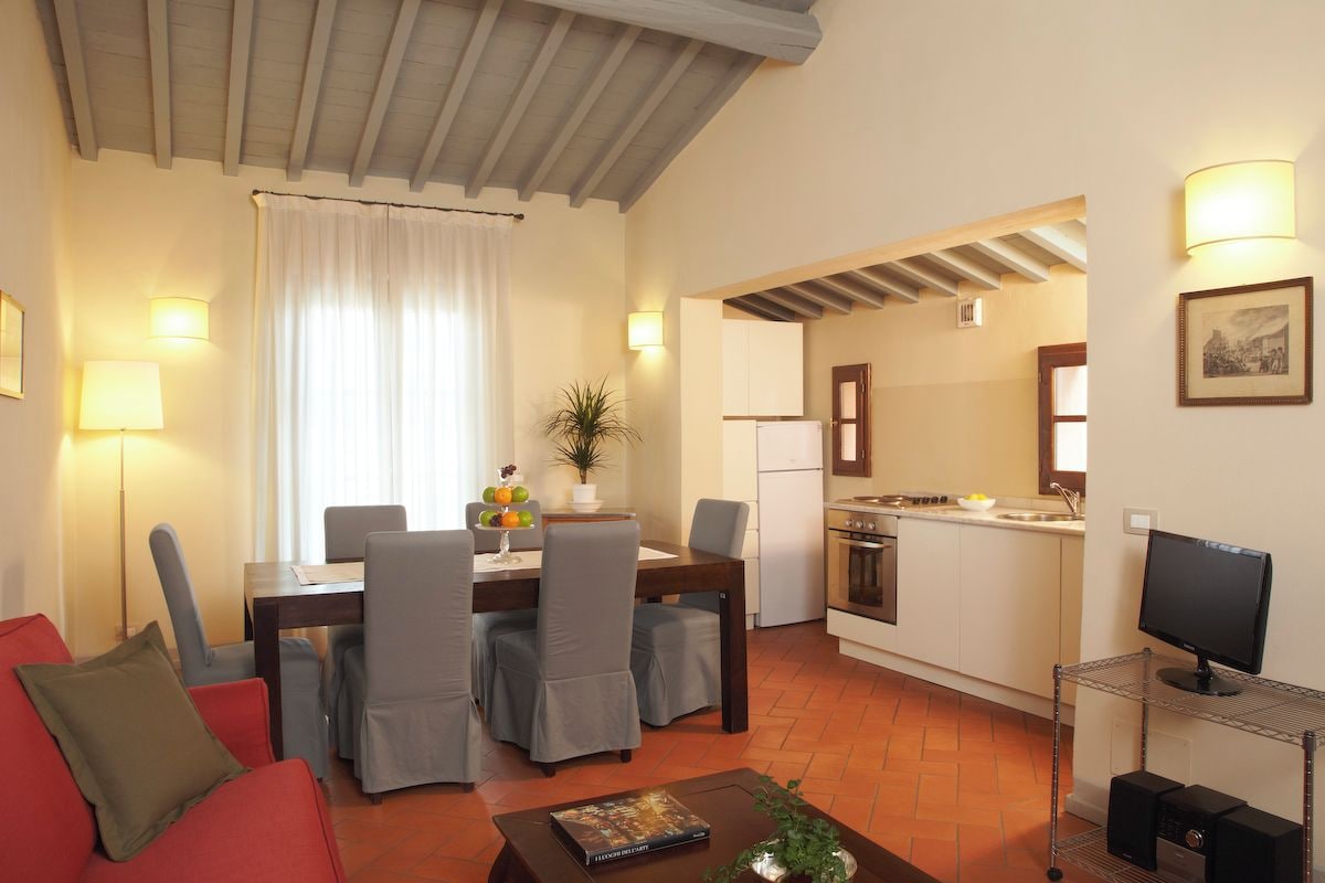 Un espacio habitable compacto con zona de comedor, kitchenette y televisor sobre un mueble.