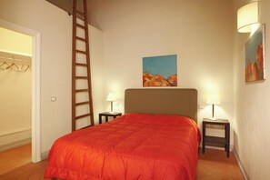 Un dormitorio con una cama, dos mesitas de noche con lámparas, una escalera, un armario y un cuadro en la pared.