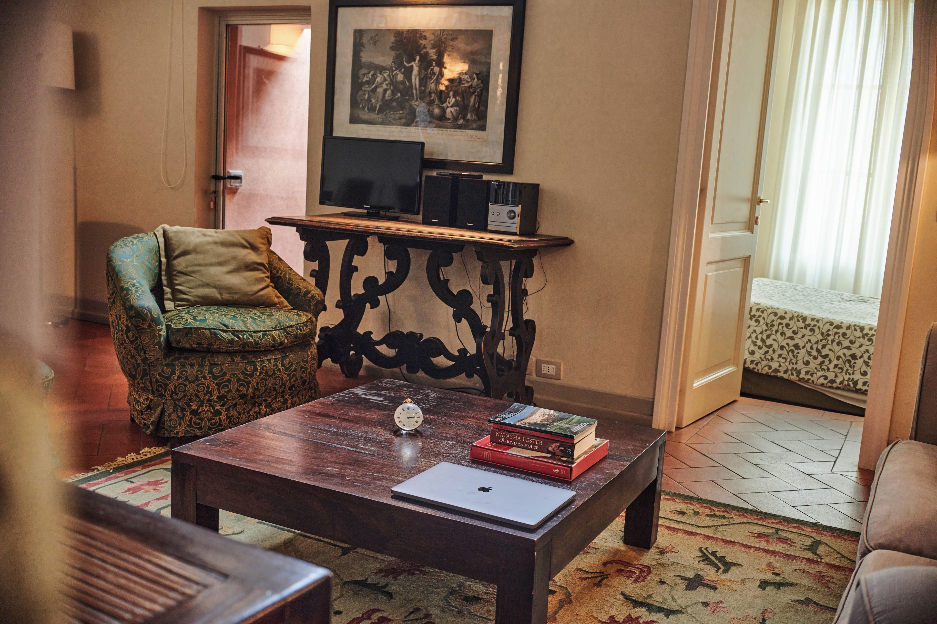 A cozy living room with a wooden coffee table, a green armchair, a side table with electronic devices, and a framed picture on the wall.