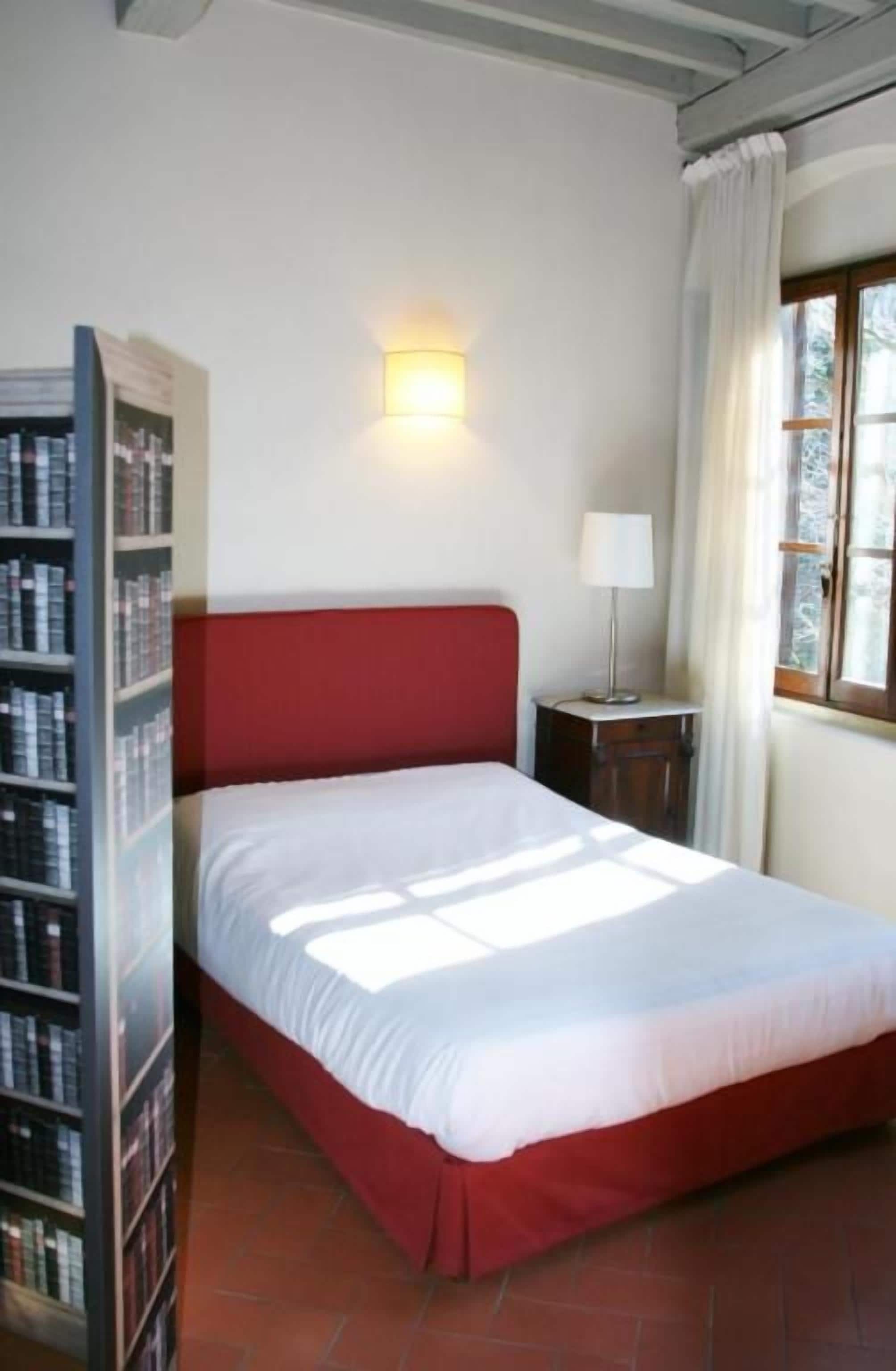 Una habitación con cama, estantería, lámpara y ventana con cortinas.
