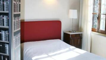 Una habitación con cama, estantería, lámpara y ventana con cortinas.