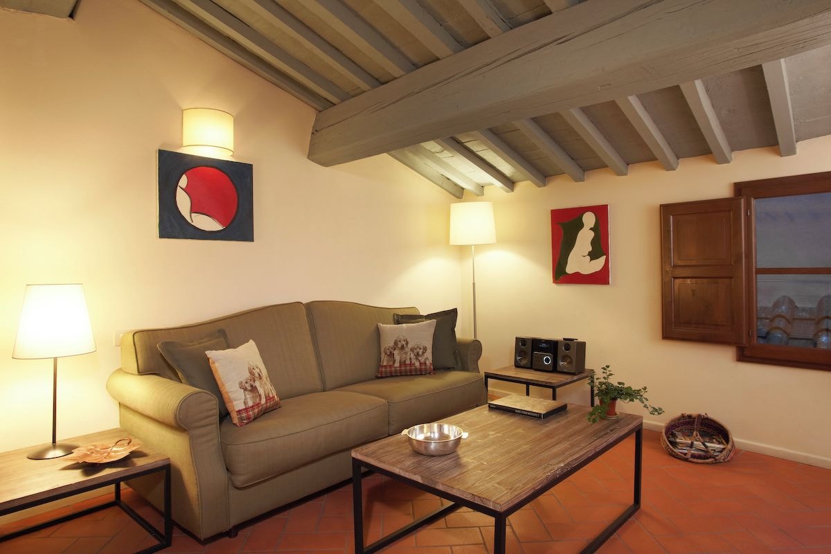 Una sala de estar con un sofá, una mesa de centro, una lámpara, un altavoz y un cuadro en la pared.