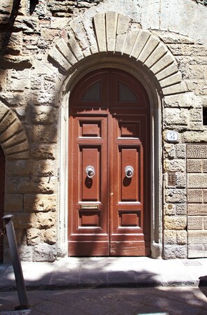 Una puerta doble de madera con un arco de piedra, un aldabón de metal y una placa con un número.